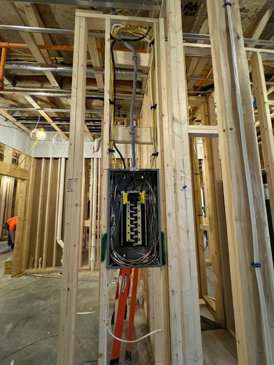 New-construction sub-panel mounted on framing with MC and Romex runs landed at the breakers.