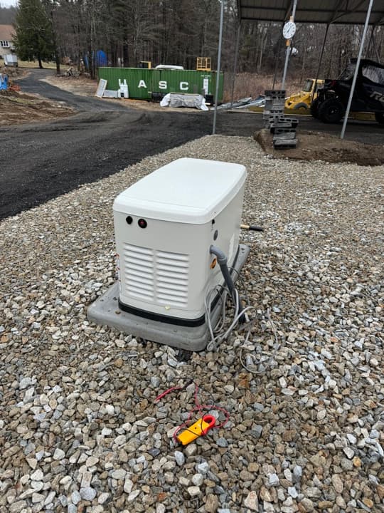 Whole-home Generac generator on a fresh gravel pad outside a residence, conduit run to the transfer switch.