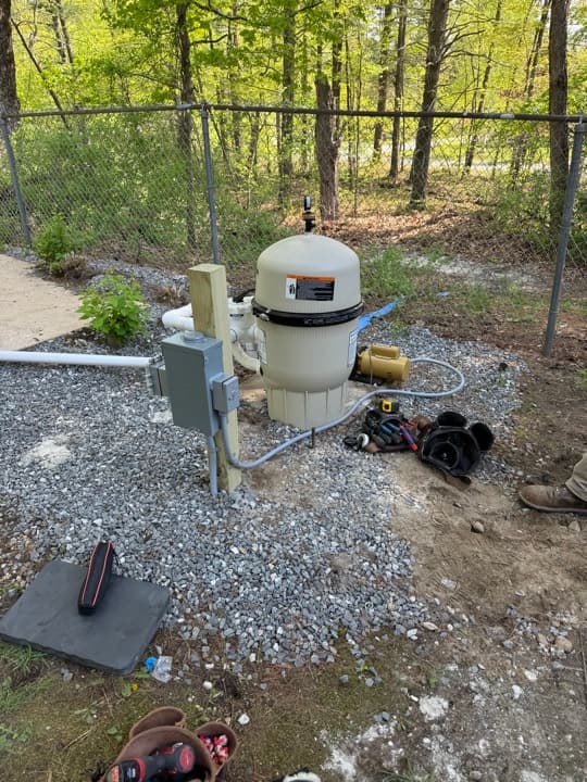Exterior pump motor with pressure switch on a stone-set pad with electrical and water plumbing.
