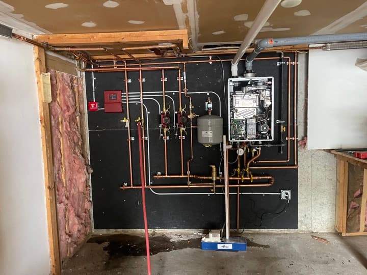 Mechanical room finished with copper hydronic loops, tankless water heater, expansion tank, and fire-alarm bell.