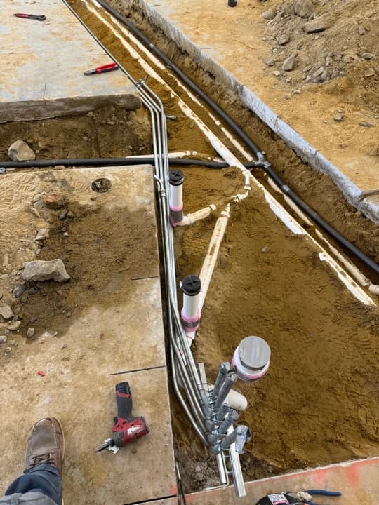 Underground service-entrance trench with sweeping PVC and rigid metal conduits transitioning into the building.