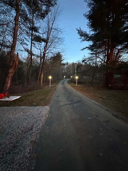 Driveway path lights illuminated at dusk along a tree-lined private drive.