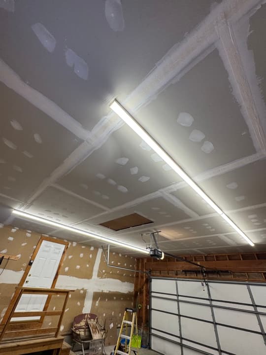 Garage at drywall stage with two long LED strip fixtures mounted on the sloped ceiling.