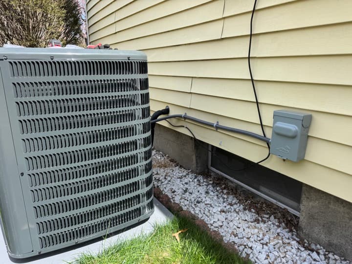 Residential air-conditioning condenser with a properly mounted service disconnect and conduit run on the wall.