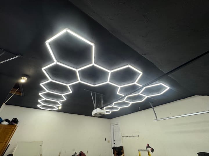 Garage ceiling with hexagonal LED light kit installed on a black-painted ceiling, fully illuminated.