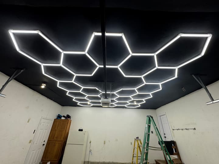 Residential garage with a hexagonal LED light kit installed on a freshly black-painted ceiling, fully illuminated and lighting the bay end-to-end.